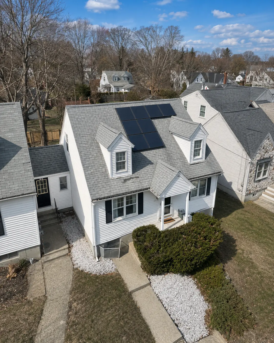 Aerial view of a white colonial-style home with rear-facing solar array